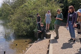 Teenagers and a member of BBOWT staff looking out over the water at the Nature Discovery Centre