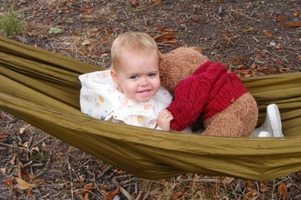 A child sits in  hammock with their teddy bear