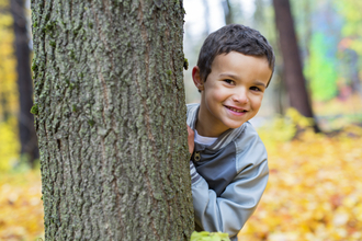 Happy young boy hiding behind a tree