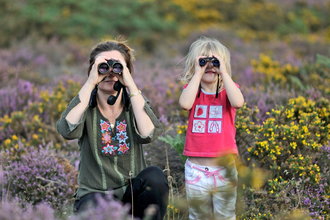 Mother and child birdwatching through binoculars surrounded by heather