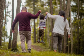 Two adults swing a child by their arms in the woods