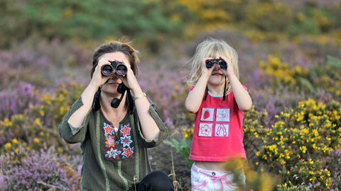 Mother and child birdwatching through binoculars surrounded by heather