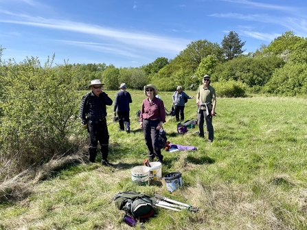 Group of volunteers standing in a grassy meadow next to small patches of scrub