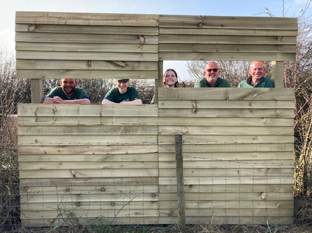 trainees and volunteers peering through wooden slatted viewing screen