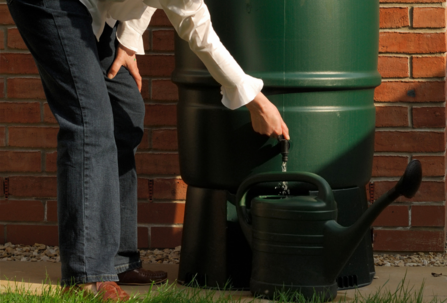 A woman filling a watering can from a green water butt