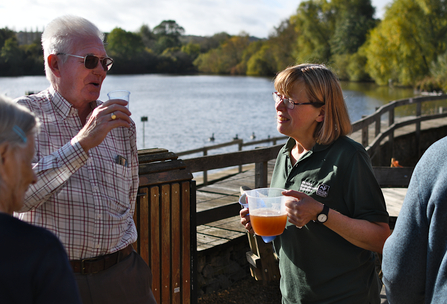 Cafe leader Jone Ayres speaking to a guest, holding a jug of fresh apple juice