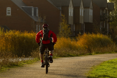 Man cycling along a path next to housing